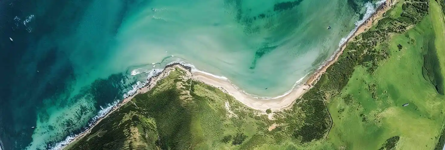 An aerial view of a coastline where the sea meets green headland